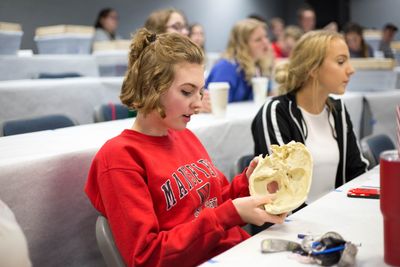 A young female student examines skeletal human remains at a table.