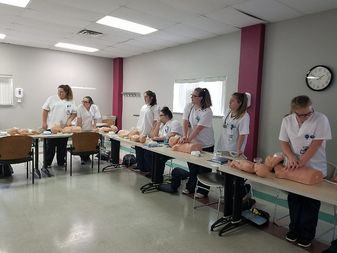 Students wearing nursing lab coats work with CPR dummies.