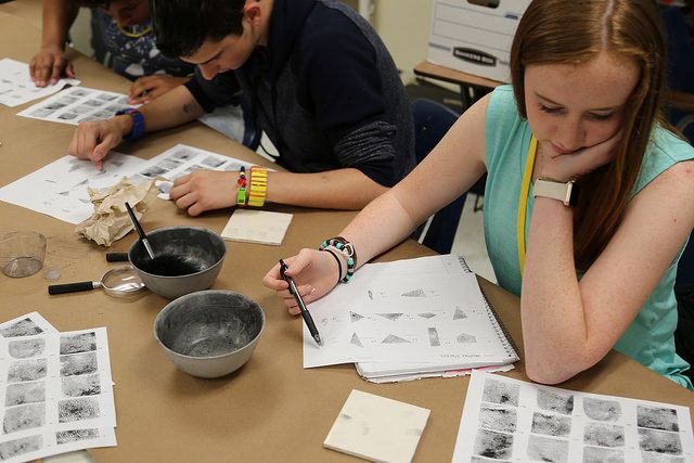 Students sit at a table where they examine sheets of paper that contain multiple fingerprints