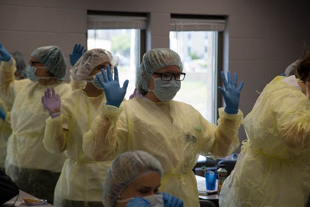 Nursing Academy students, dressed in emergency rooms scrubs, lift their gloved hands for inspection as professors ensure they are properly dressed.